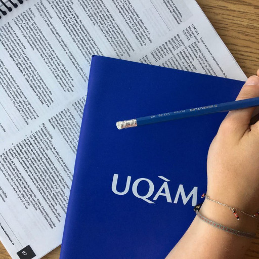 Une main tenant un crayon de plomb au-dessus d'un livre UQAM