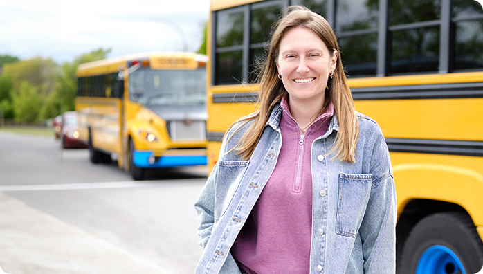 Intervenante du milieu scolaire souriante devant des autobus jaunes, illustrant la formation continue et le développement professionnel en éducation.